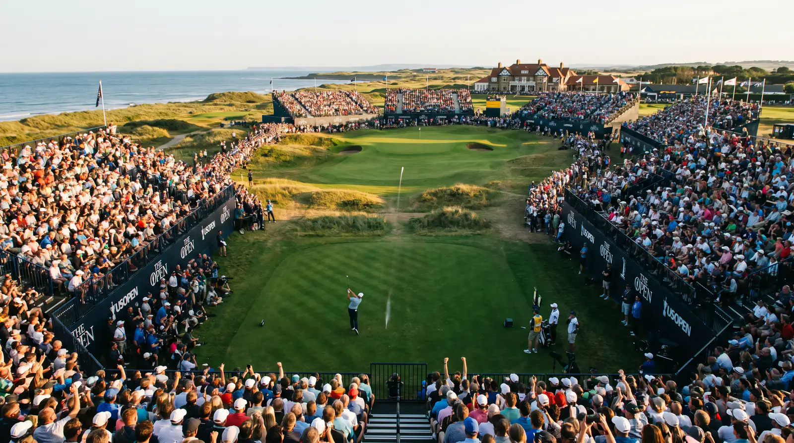 Spectators gathered around a par-three hole watching professional golfers tee off during a major championship