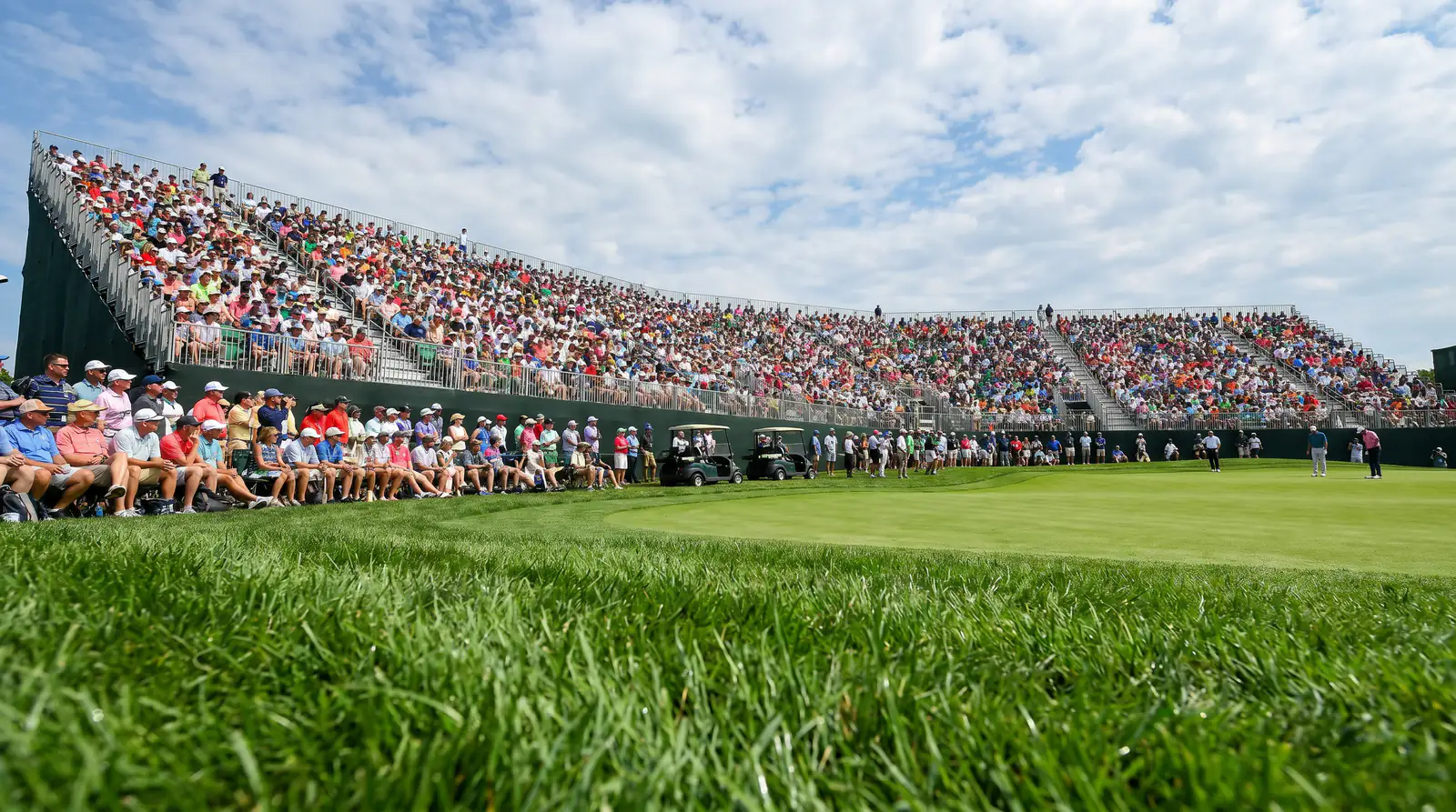 Packed grandstand at a major championship golf tournament with spectators watching the green