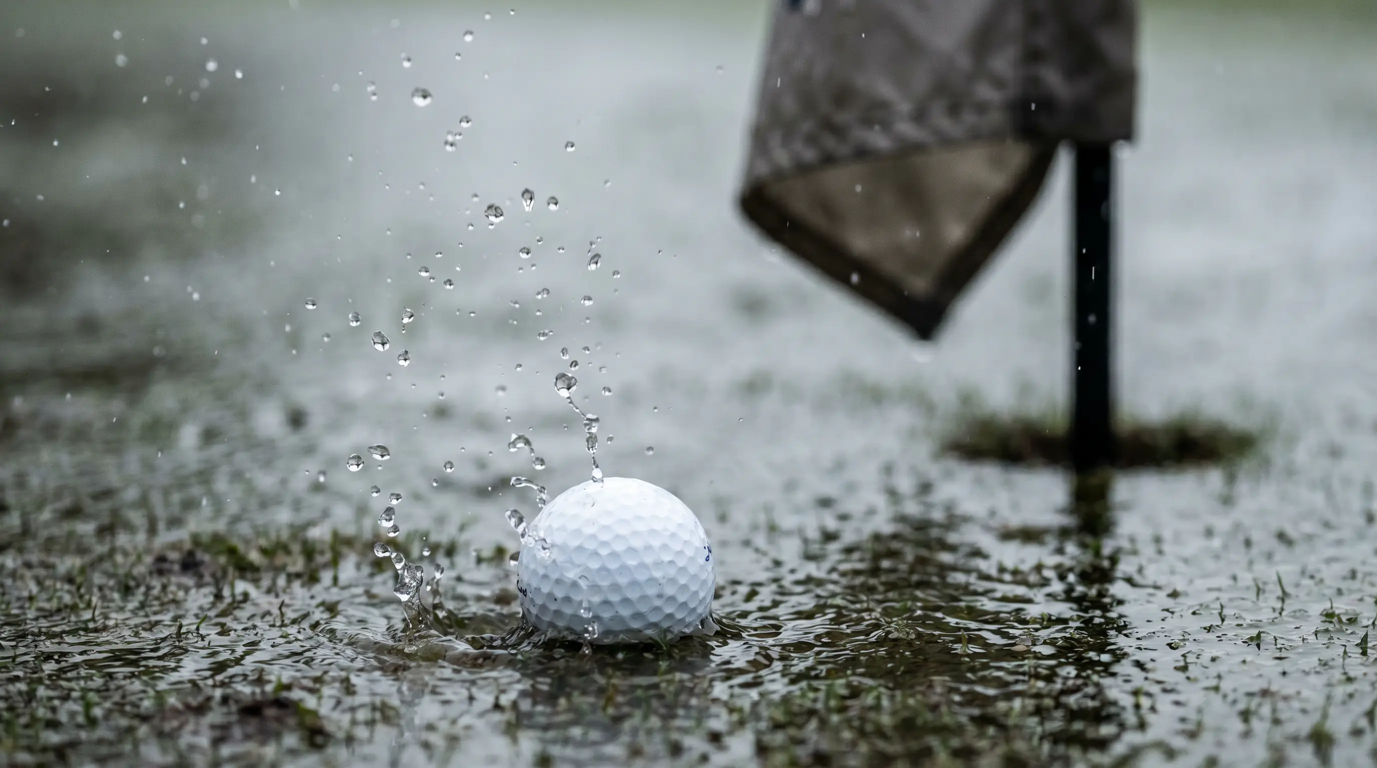 Golf ball landing on a rain-soaked green with water splashing on impact during wet conditions