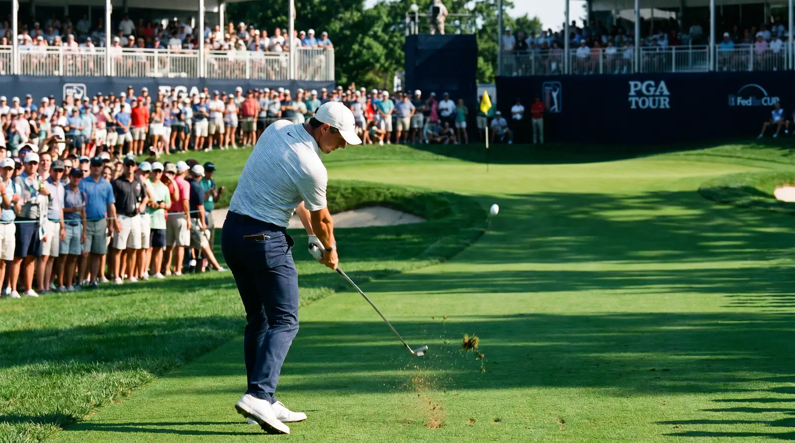 Golfer hitting an iron approach shot toward the green during a professional tournament